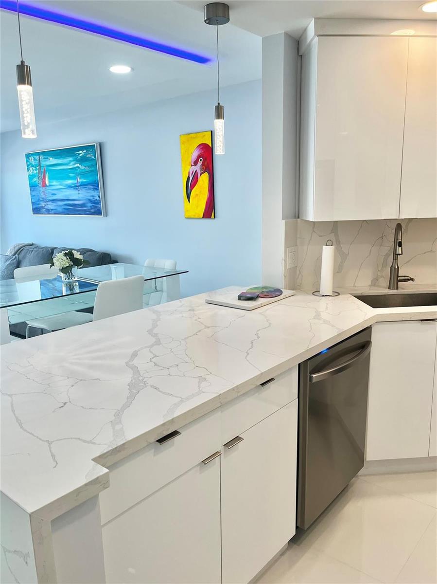 A modern kitchen features white cabinets, marble-patterned countertops, and a view into the dining area — 133 N Pompano Beach Boulevard # 105, Pompano Beach FL 33062, POMPANO BEACH, FL