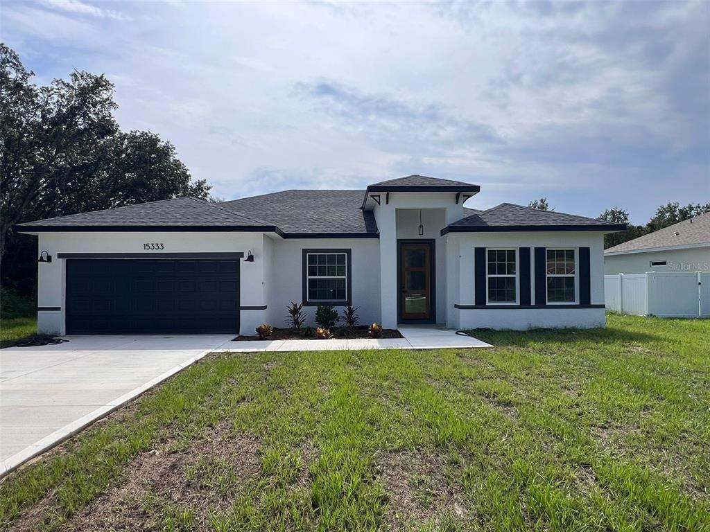 A single-story house with a white stucco exterior, dark trim, and a two-car garage — 15333 SW 59TH AVENUE RD, OCALA, FL