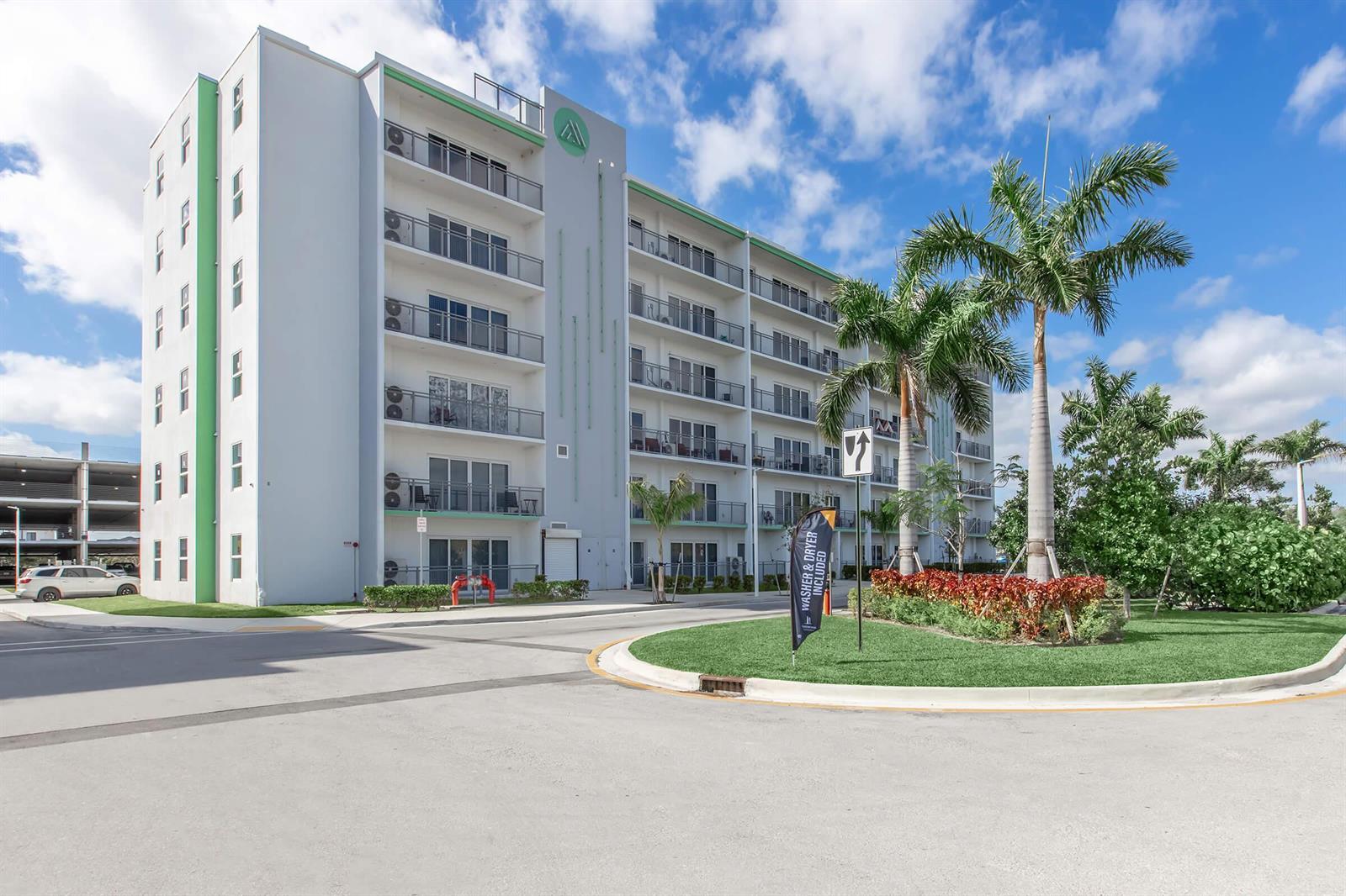 A multi-story apartment building with balconies and palm trees stands under a blue sky — 25885 S Dixie Highway, Homestead FL 33032, HOMESTEAD, FL
