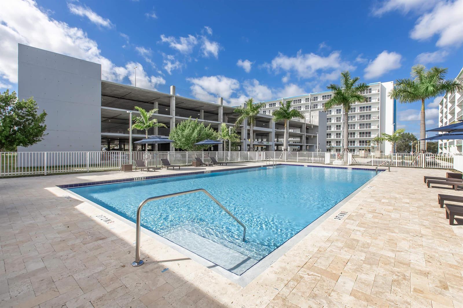 A rectangular swimming pool sits on a stone patio in front of a parking garage — 25885 S Dixie Highway, Homestead FL 33032, HOMESTEAD, FL