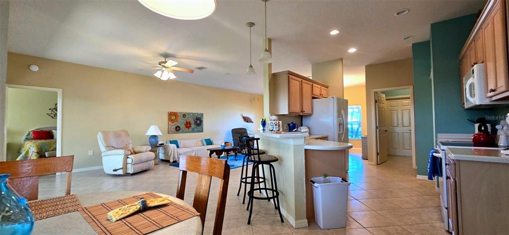 An open-concept kitchen and living area features tile flooring, light wood cabinets, and bar seating — 4023 ASHTON CLUB DRIVE, LAKE WALES, FL