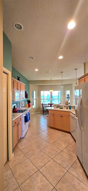 A kitchen with light wood cabinets, tile flooring, and a dining area with large windows — 4023 ASHTON CLUB DRIVE, LAKE WALES, FL