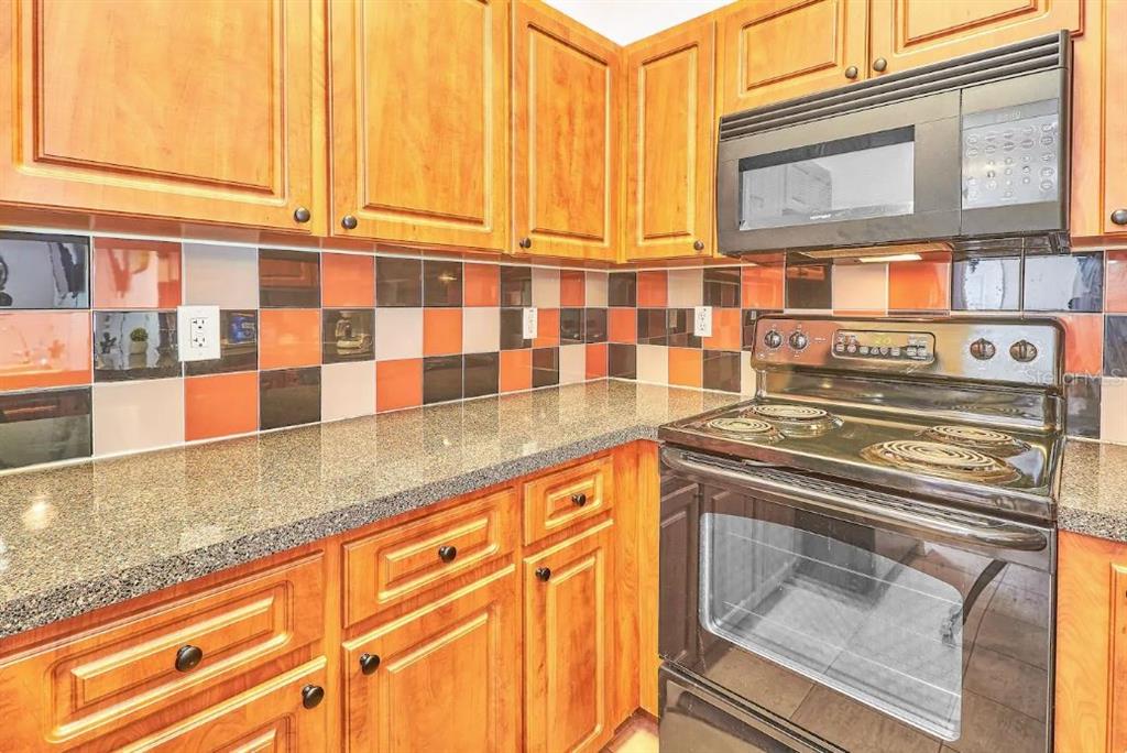 A kitchen features wood cabinets, a granite countertop, a black stove, and a multicolored backsplash — 800 E BAKER STREET, TAMPA, FL