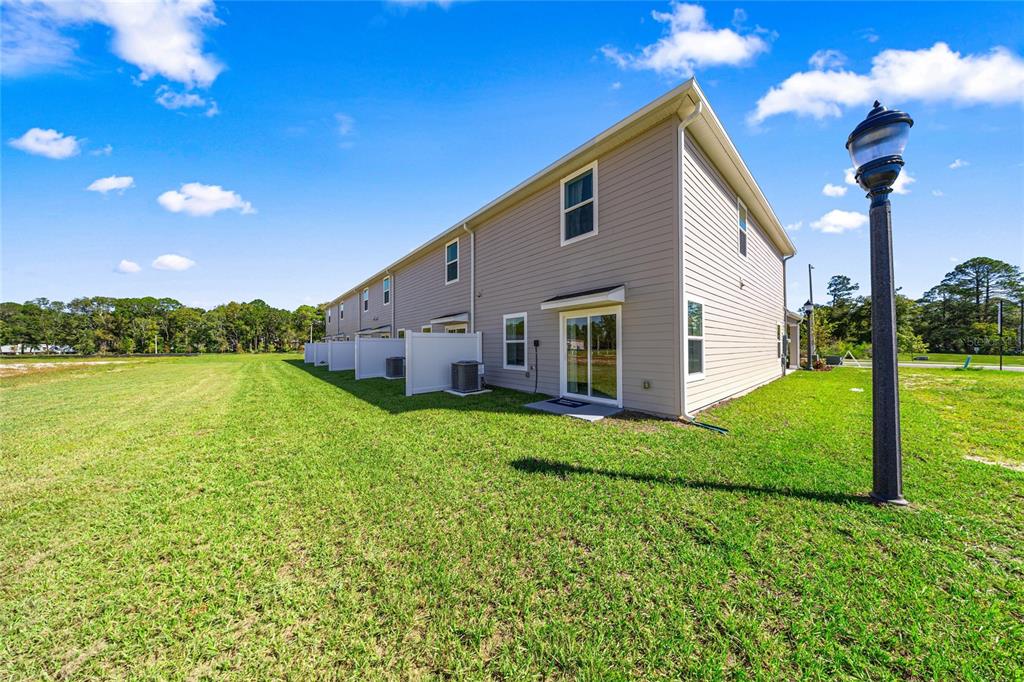 The exterior of a multi-unit townhouse building features light-colored siding and a grassy backyard — 5422 NW 22ND DRIVE, GAINESVILLE, FL