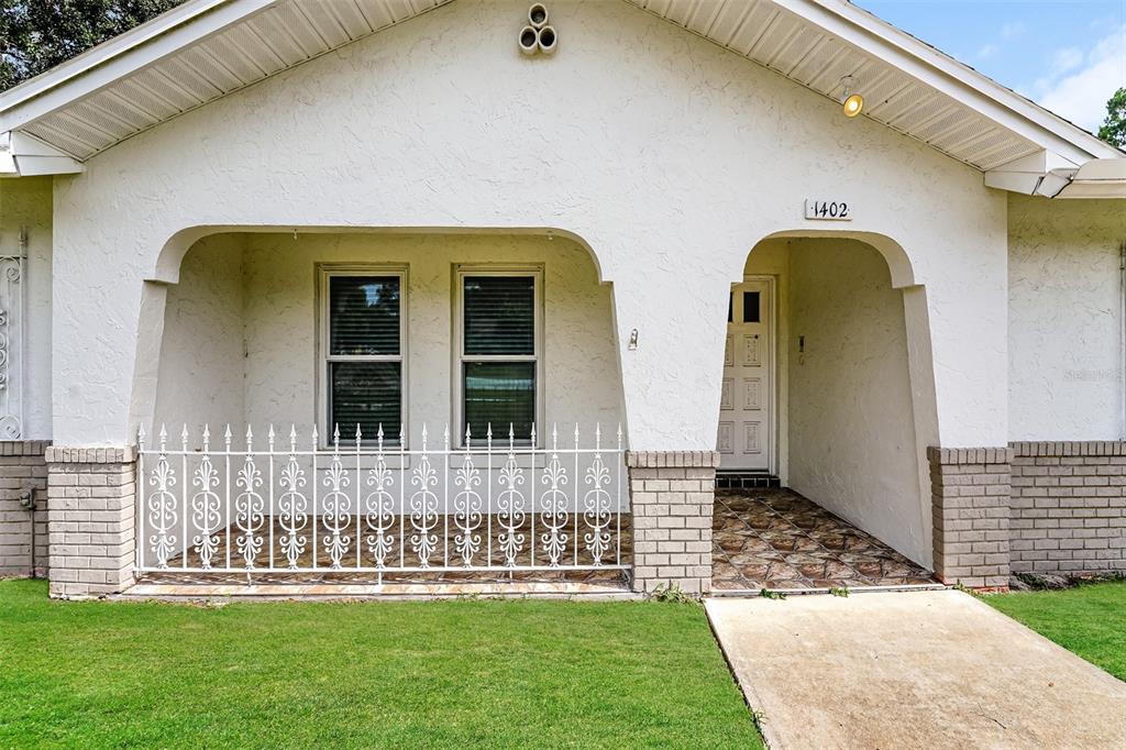 A white house exterior features a covered front porch with a decorative metal railing — 1402 FINDLAY STREET, DELTONA, FL