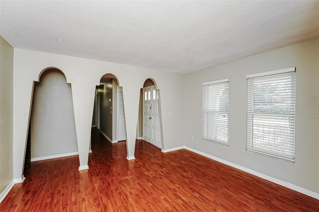 A room with wood-look flooring, light-colored walls, two windows with blinds, and three arched openings — 1402 FINDLAY STREET, DELTONA, FL