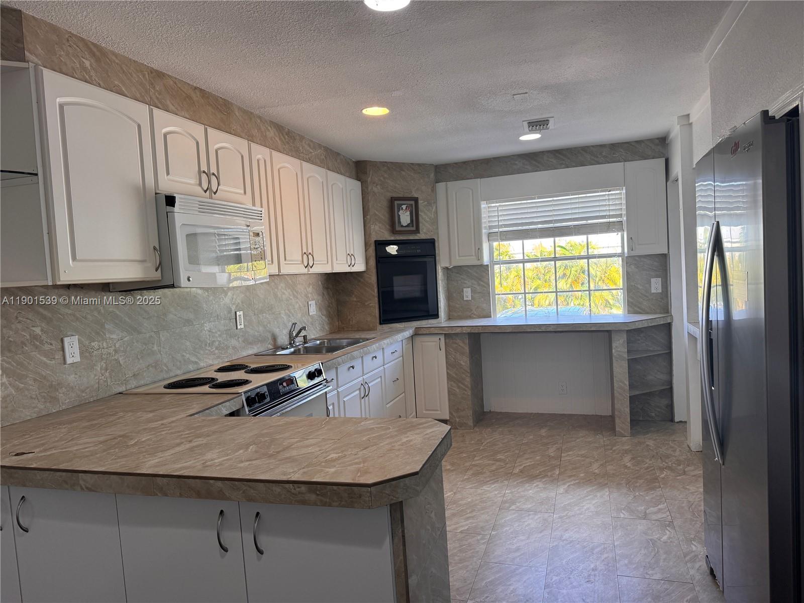 A kitchen features white cabinets, marble-patterned countertops and backsplash, and stainless steel appliances — 969 Plantation Rd, Key Largo FL 33037, KEY LARGO, FL