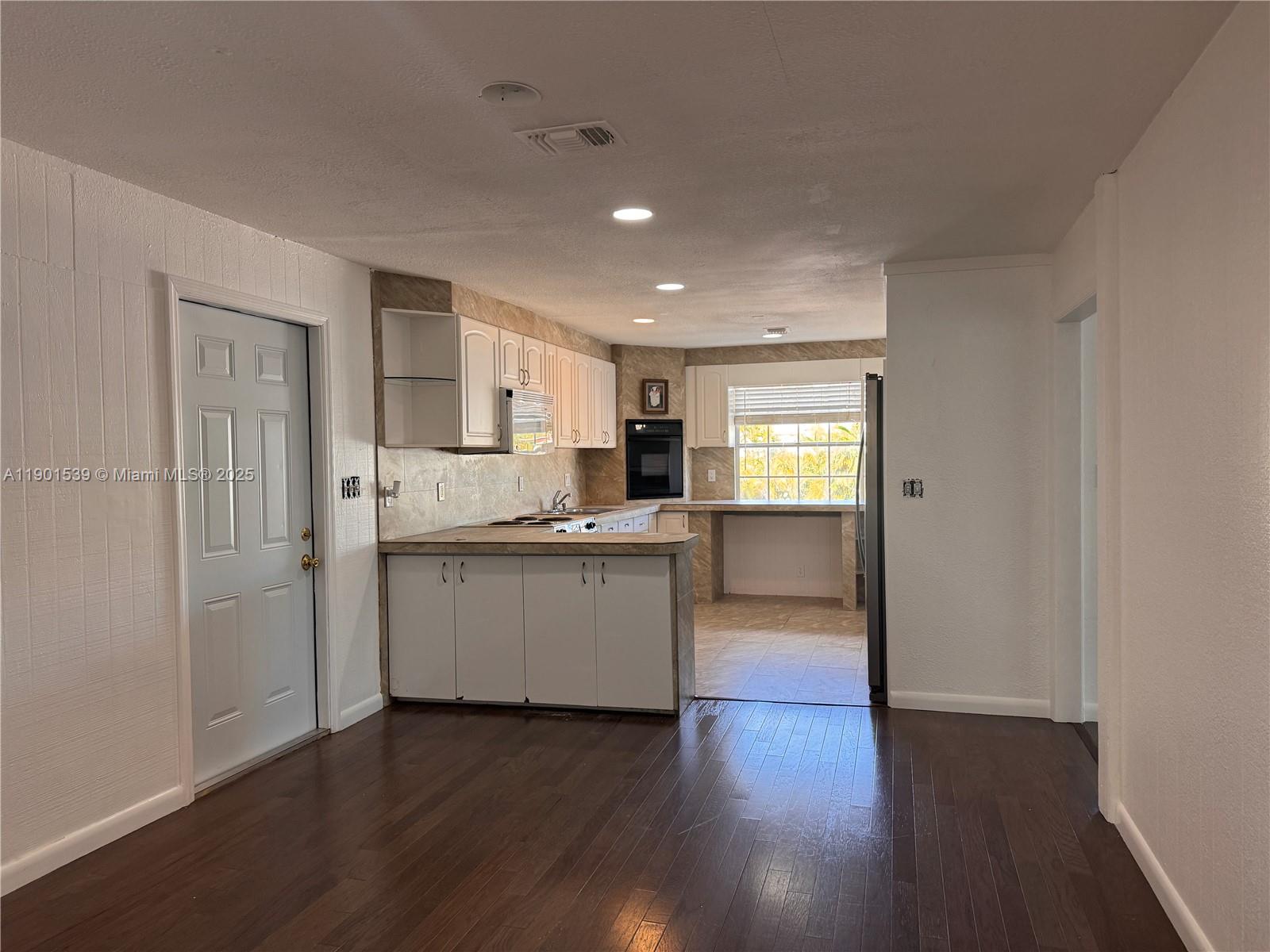 A kitchen features white cabinets, a peninsula, and dark wood flooring in the adjacent area — 969 Plantation Rd, Key Largo FL 33037, KEY LARGO, FL