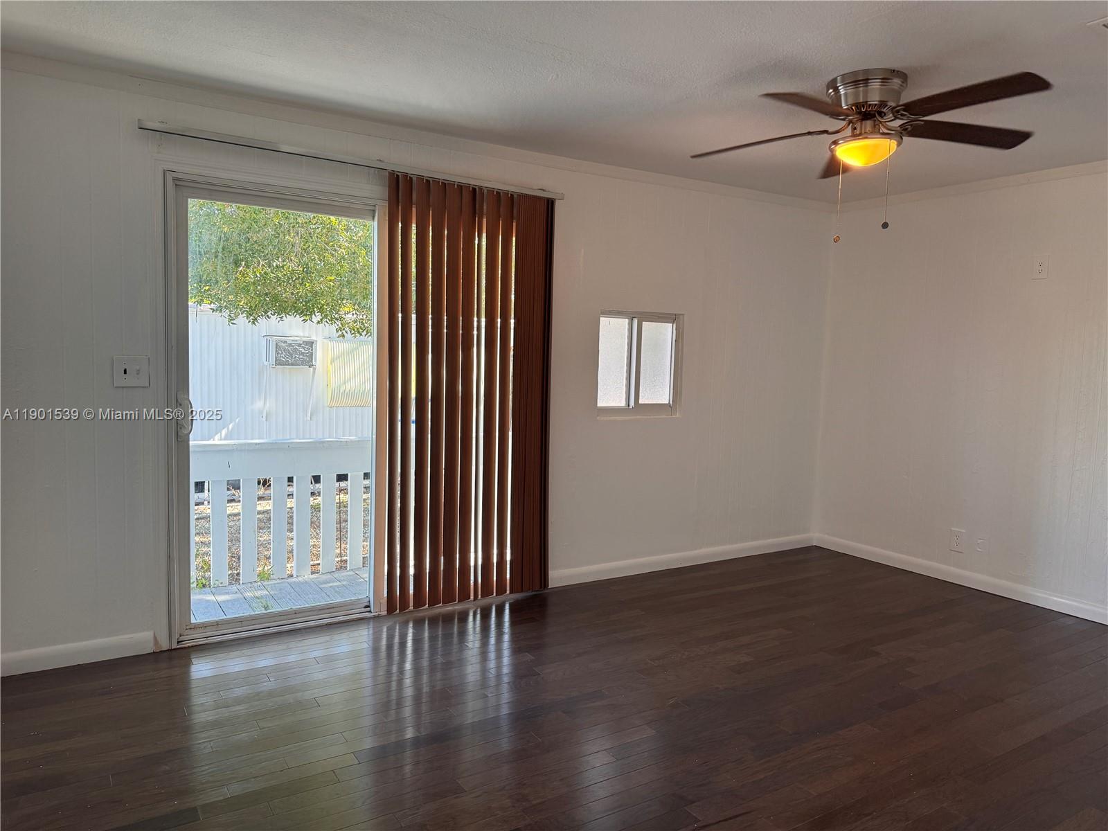 An empty room features dark wood flooring, a ceiling fan, and a sliding glass door — 969 Plantation Rd, Key Largo FL 33037, KEY LARGO, FL