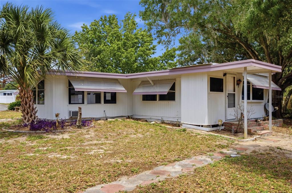 A single-story mobile home with white siding, metal awnings, and a palm tree in front — 14742 MANDARIN STREET, TAVARES, FL