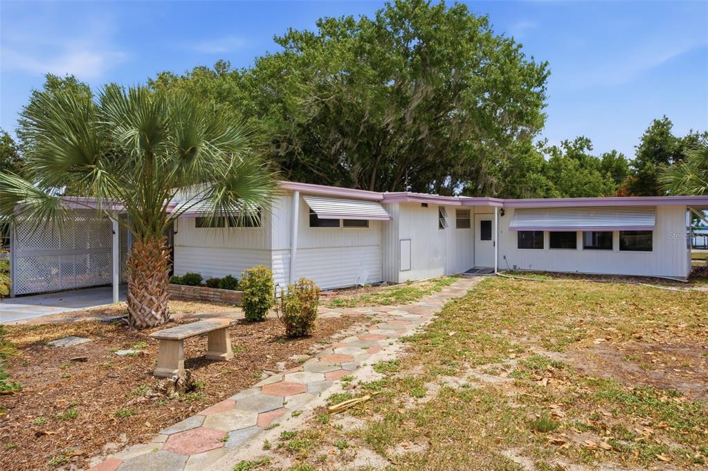 A single-story white mobile home with a metal awning, palm tree, and stone walkway — 14742 MANDARIN STREET, TAVARES, FL