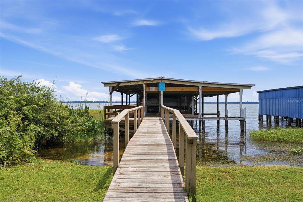 A wooden walkway leads to a covered boat dock on a lake under a blue sky — 14742 MANDARIN STREET, TAVARES, FL