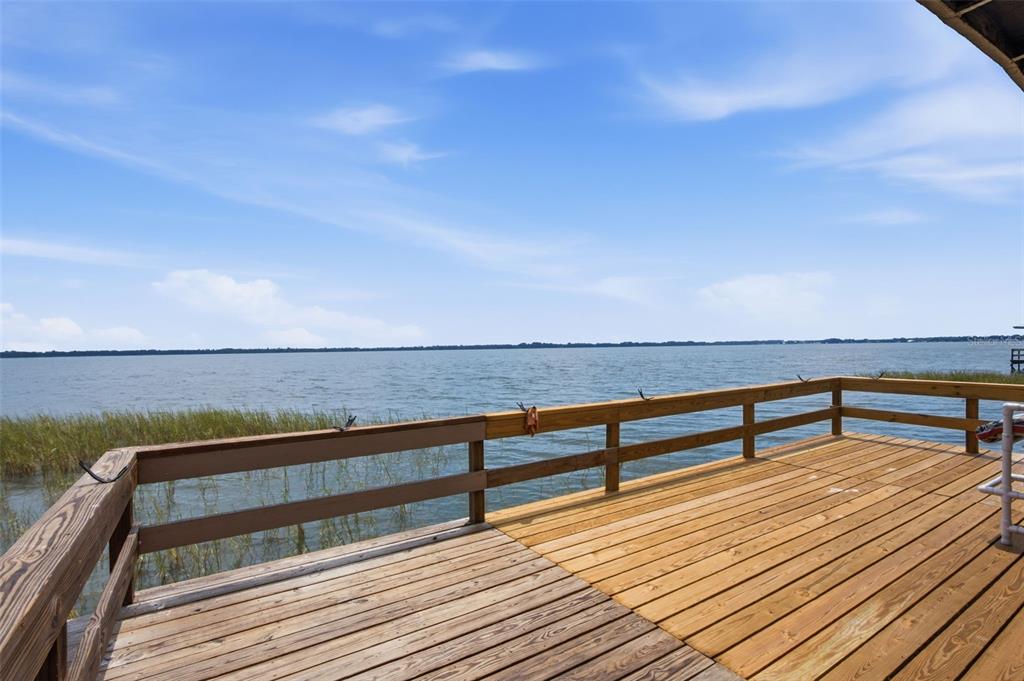 A wooden deck with railings overlooks a large lake under a blue sky — 14742 MANDARIN STREET, TAVARES, FL