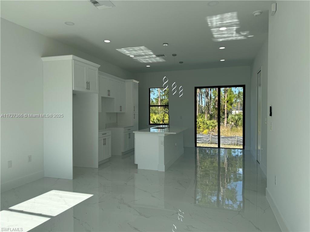 A modern kitchen with white cabinets and an island features light-colored tile flooring — 3002 68th ST W, Lehigh Acres FL 33971, LEHIGH ACRES, FL