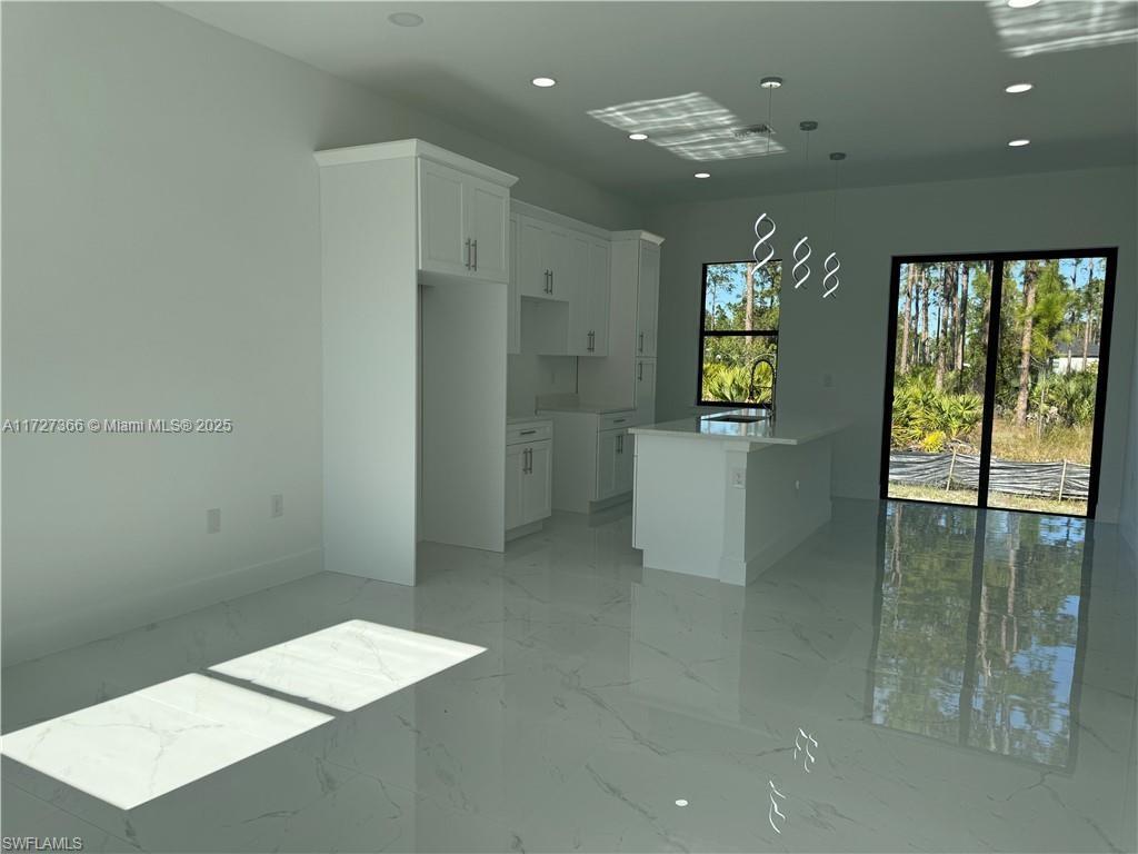 A modern kitchen features white cabinetry, a center island, and glossy marble-look tile flooring — 3002 68th ST W, Lehigh Acres FL 33971, LEHIGH ACRES, FL