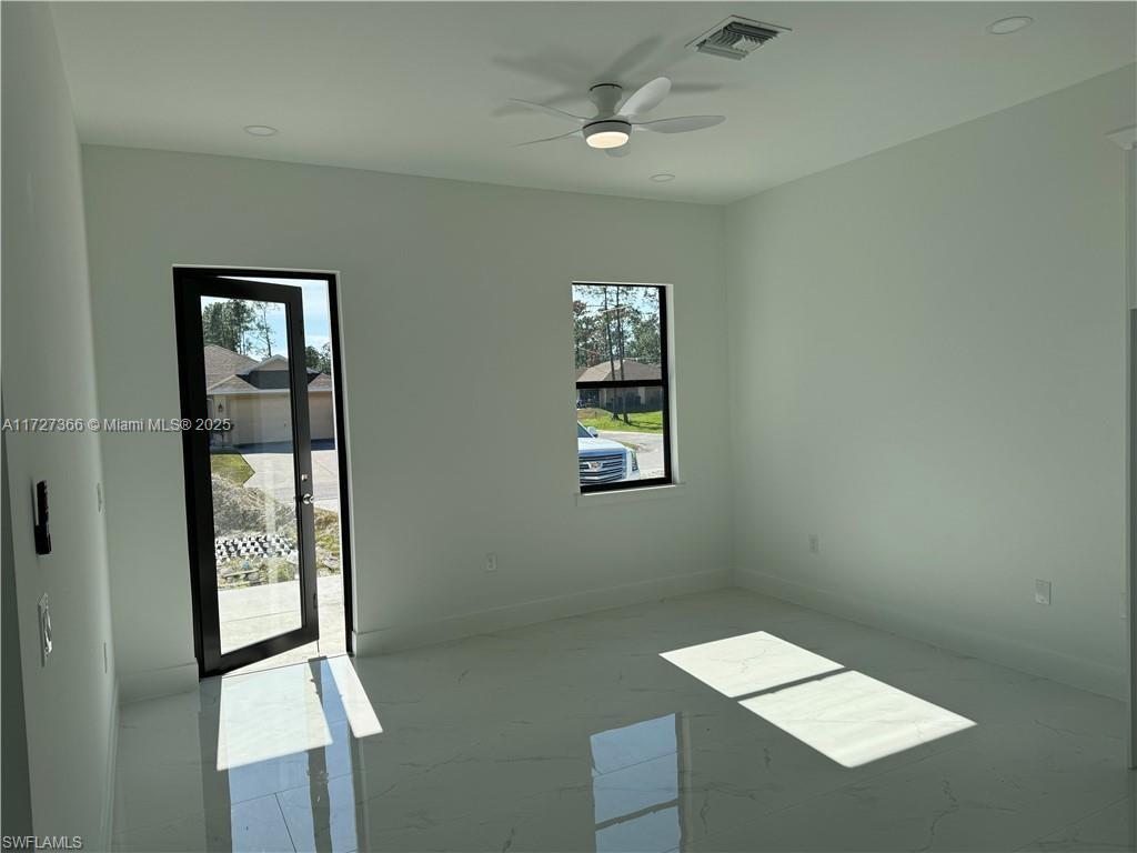 A bright, empty room features white walls, white tile flooring, a ceiling fan, and a door — 3002 68th ST W, Lehigh Acres FL 33971, LEHIGH ACRES, FL