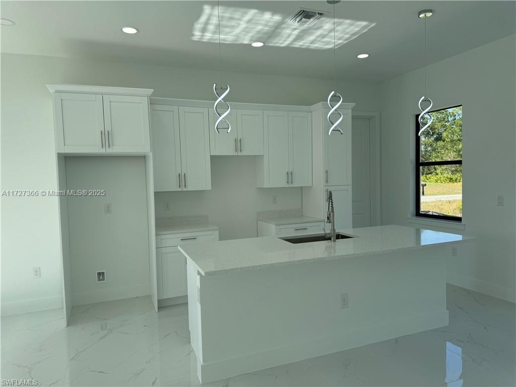 A modern kitchen features white cabinetry, a quartz island with a sink, and marble flooring — 3002 68th ST W, Lehigh Acres FL 33971, LEHIGH ACRES, FL