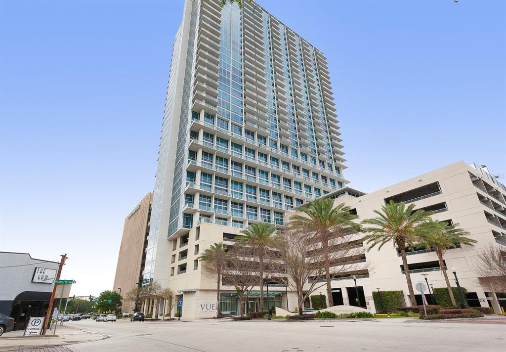 A tall glass residential tower stands next to a multi-level parking garage with palm trees — 150 E ROBINSON STREET UNIT 2012, ORLANDO, FL