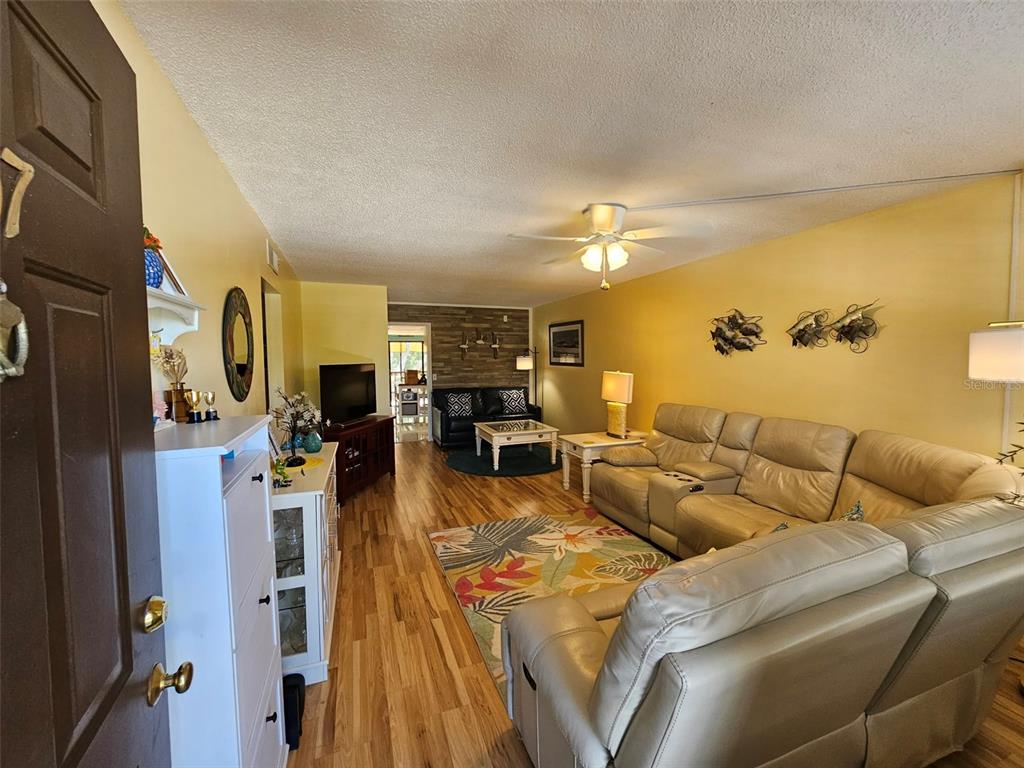 A living room features light wood flooring, yellow walls, a ceiling fan, and leather furniture — 315 30TH AVENUE W UNIT B307, BRADENTON, FL