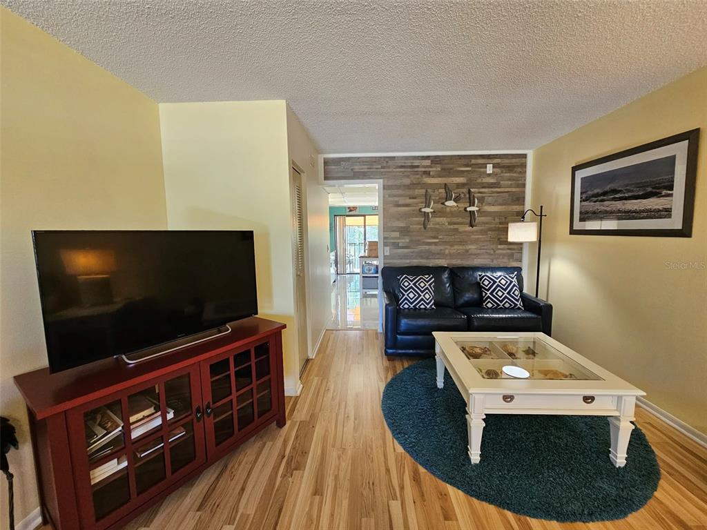 A living room features a television console, a dark sofa, and a glass-topped coffee table — 315 30TH AVENUE W UNIT B307, BRADENTON, FL