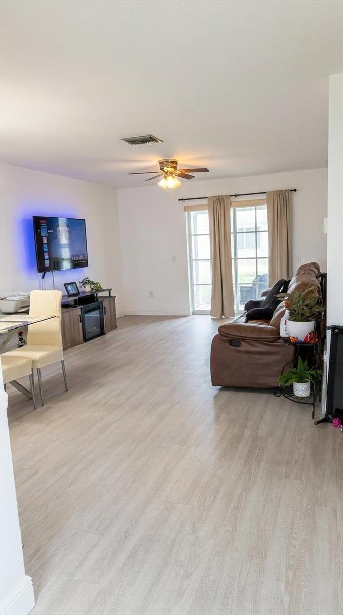 A living room features light wood-look flooring, a brown leather sofa, and a wall-mounted television — 2898 Ashley Dr Drive E # C, West Palm Beach FL 33415, WEST PALM BEACH, FL
