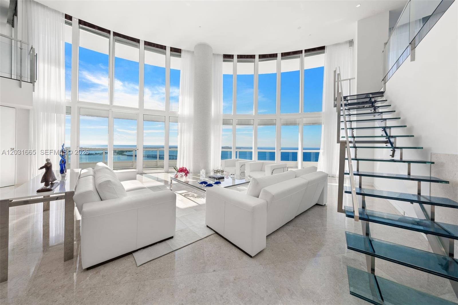 A modern living room features floor-to-ceiling windows, white sofas, and a glass staircase — 1643 Brickell Ave # 4102, Miami FL 33129, MIAMI, FL