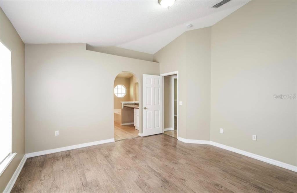 An empty bedroom features light-colored walls, wood-look flooring, and an arched doorway to a bathroom — 1131 EVENING TRAIL DRIVE, WESLEY CHAPEL, FL
