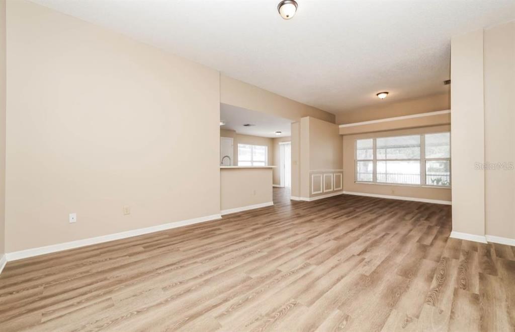 An empty living room features light-colored walls, wood-look flooring, and a large window — 1131 EVENING TRAIL DRIVE, WESLEY CHAPEL, FL