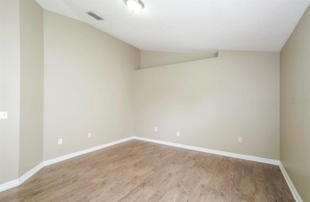 An empty room with beige walls, wood-look flooring, and a vaulted ceiling — 1131 EVENING TRAIL DRIVE, WESLEY CHAPEL, FL