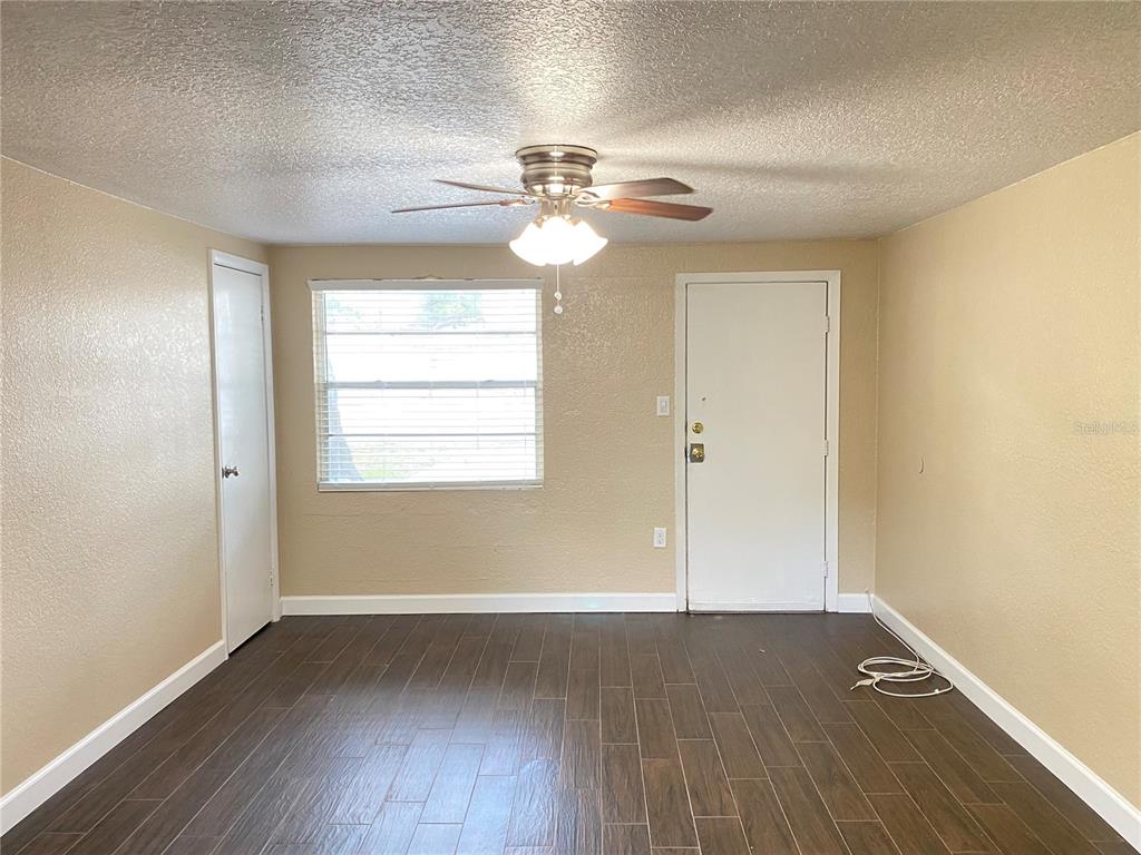An empty room features dark wood-look flooring, beige walls, a ceiling fan, and a window — 37147 MARLU LANE, DADE CITY, FL