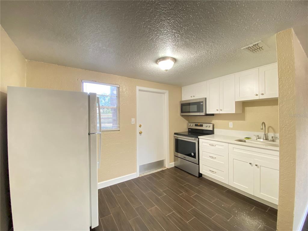 A kitchen features white cabinets, stainless steel appliances, and dark wood-look tile flooring — 37147 MARLU LANE, DADE CITY, FL