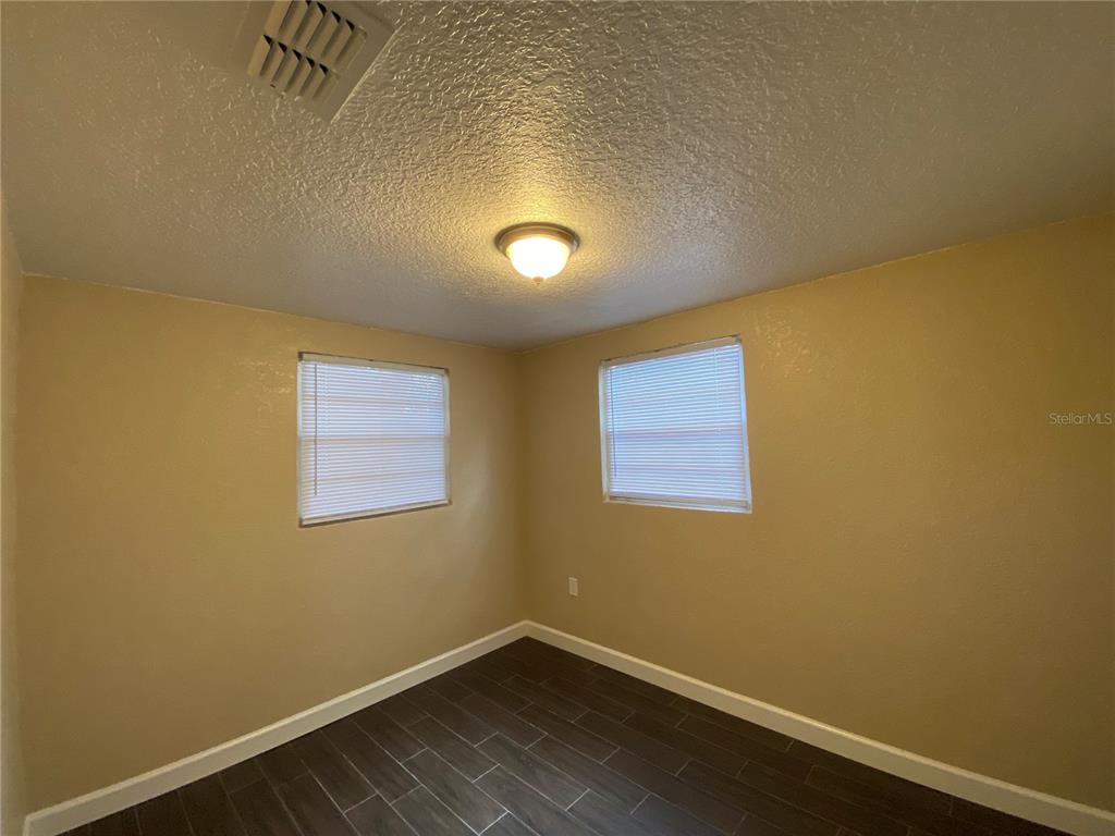 A bedroom with tan walls, dark wood-look tile flooring, and two windows with blinds — 37147 MARLU LANE, DADE CITY, FL