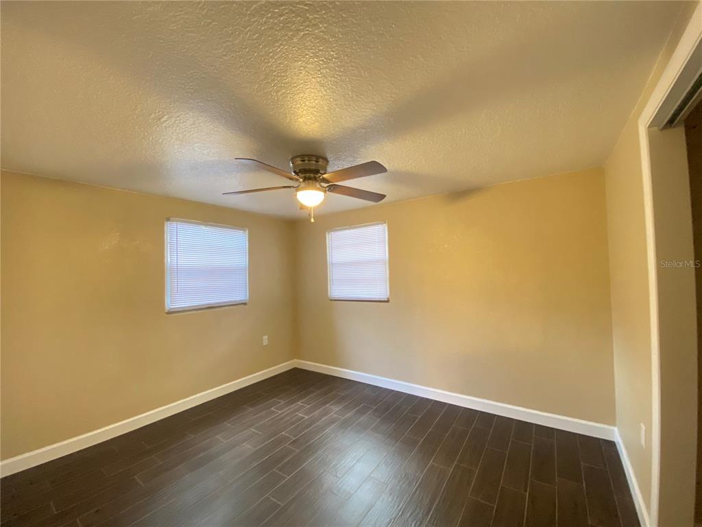 An empty bedroom features tan walls, dark wood-look tile flooring, and a ceiling fan — 37147 MARLU LANE, DADE CITY, FL