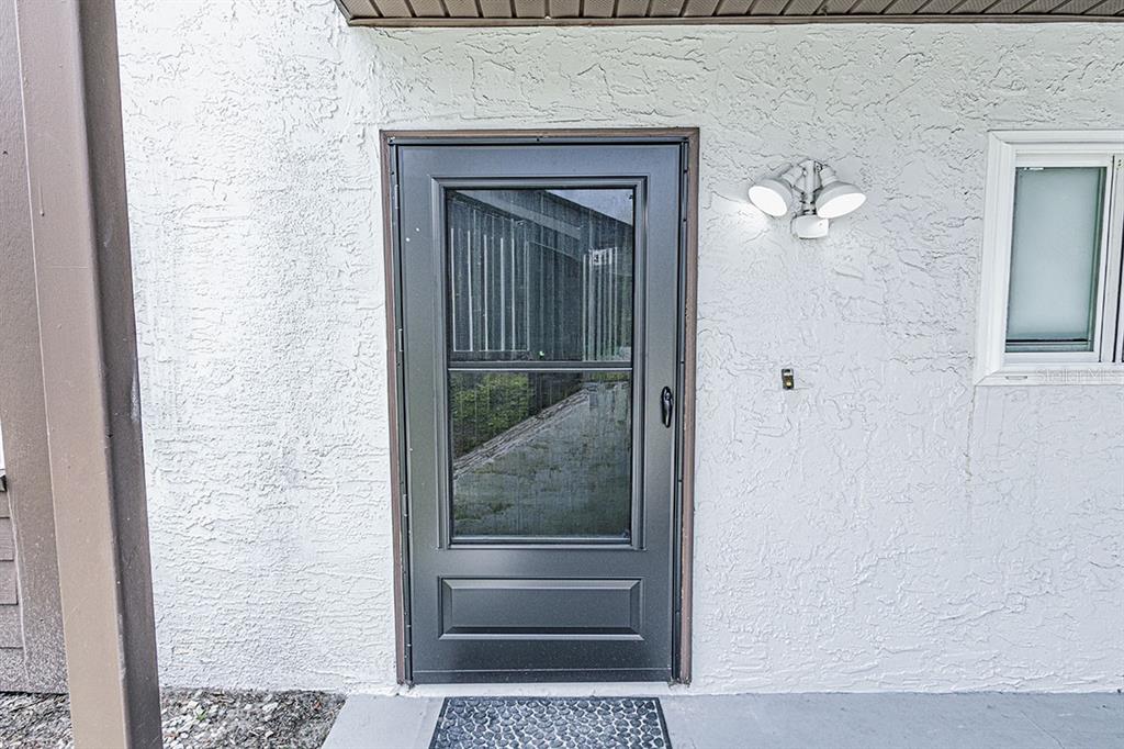 A dark storm door is installed on a white stucco exterior wall next to a window — 39132 COUNTY ROAD 54 UNIT 2172, ZEPHYRHILLS, FL