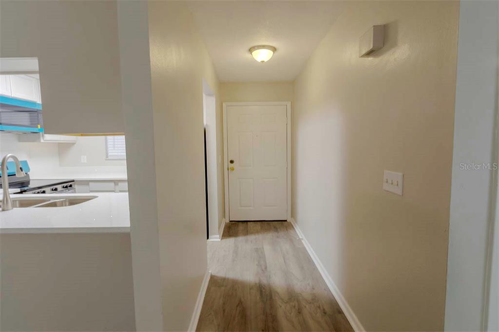 A hallway with light wood-look flooring leads to a white door under a ceiling light — 39132 COUNTY ROAD 54 UNIT 2172, ZEPHYRHILLS, FL