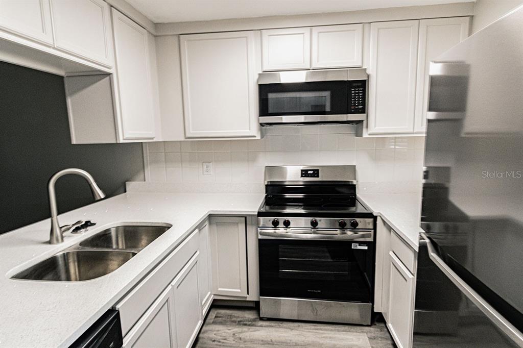 A kitchen features white cabinets, stainless steel appliances, a double sink, and light countertops — 39132 COUNTY ROAD 54 UNIT 2172, ZEPHYRHILLS, FL