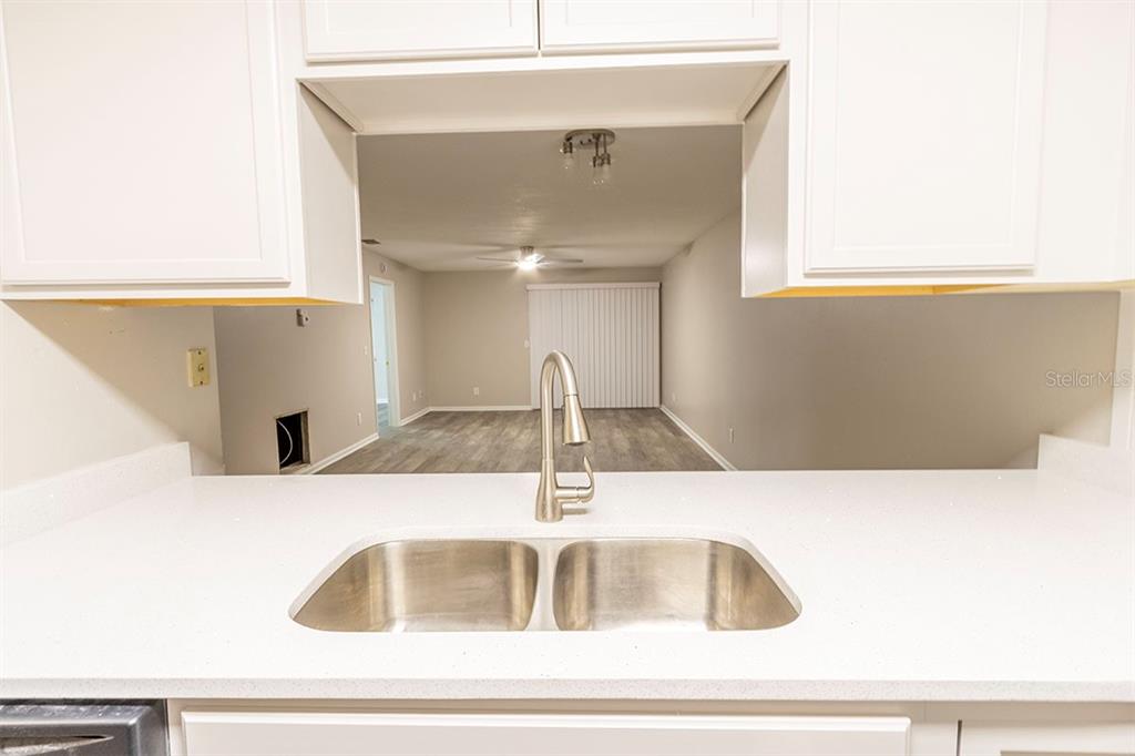 A kitchen sink and countertop overlook an open-concept living area with wood-look flooring — 39132 COUNTY ROAD 54 UNIT 2172, ZEPHYRHILLS, FL
