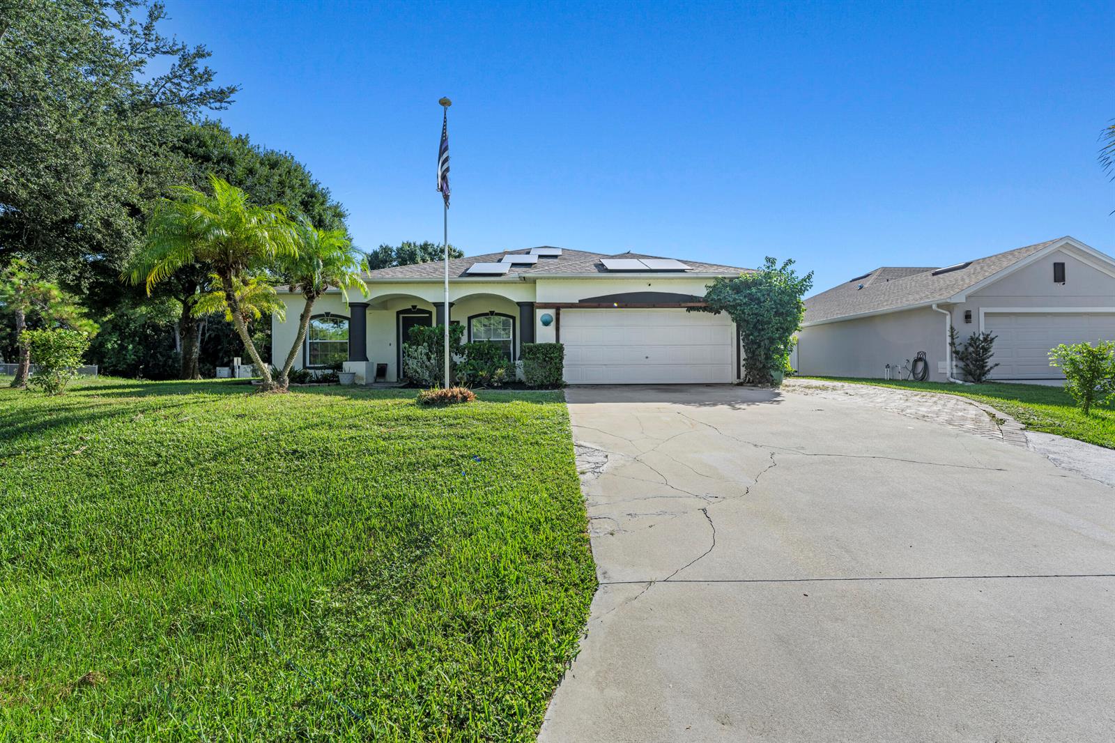A single-story house with a white garage, solar panels, and a flagpole on the lawn — 1302 Coverbrook Lane, Sebastian FL 32958, SEBASTIAN, FL