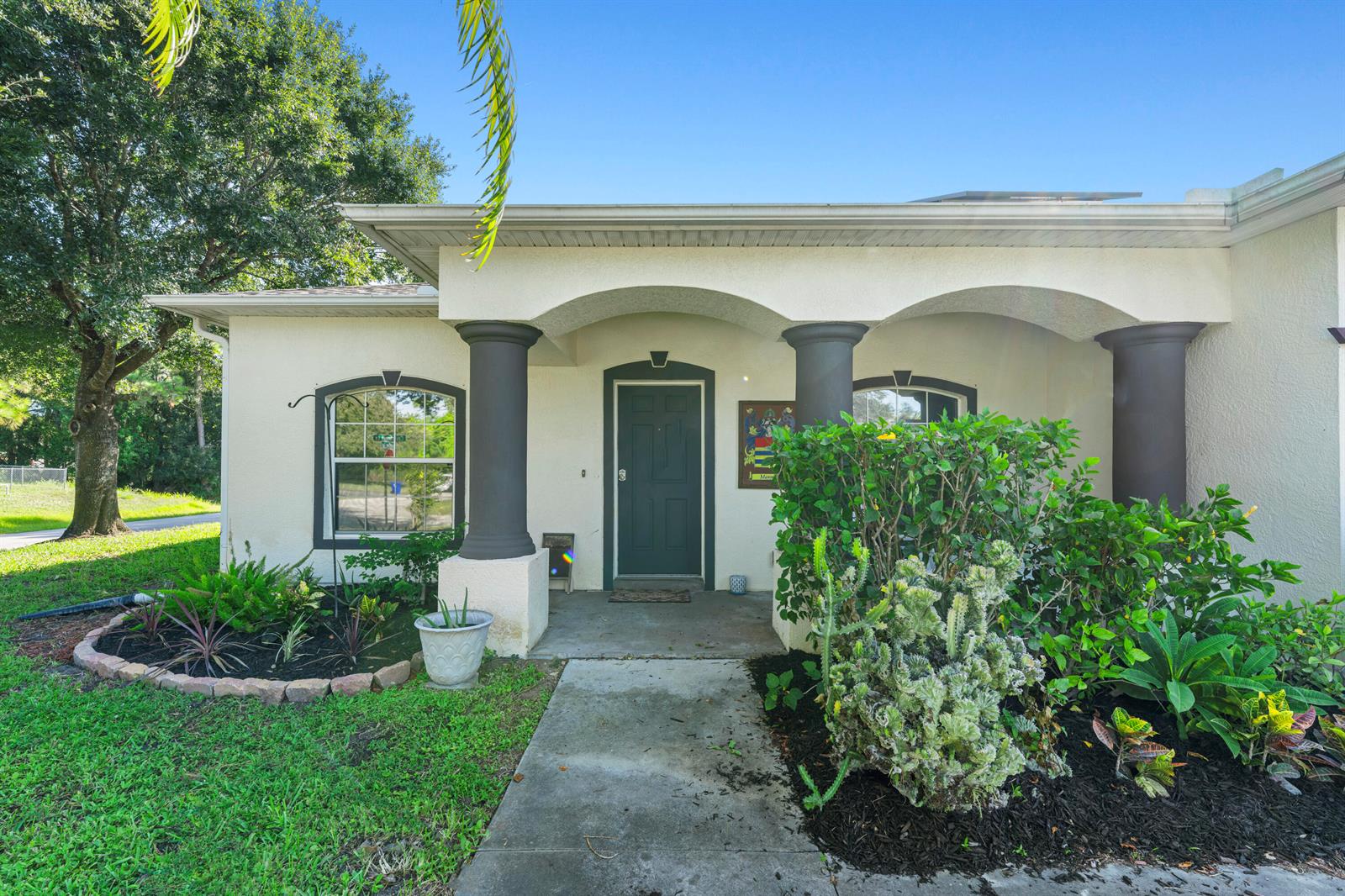 The exterior of a house features a covered porch with dark columns and a green door — 1302 Coverbrook Lane, Sebastian FL 32958, SEBASTIAN, FL