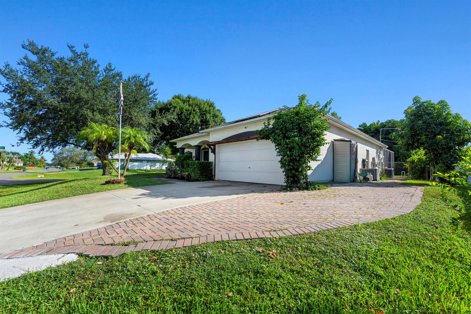 A single-story house features a white garage, a brick driveway, and a large green tree — 1302 Coverbrook Lane, Sebastian FL 32958, SEBASTIAN, FL