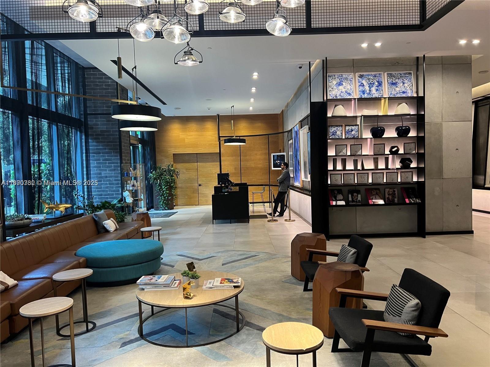 A modern lobby features a brown leather sofa, black armchairs, and a large display shelf — 121 NE 34th St # 1610, Miami FL 33137, MIAMI, FL
