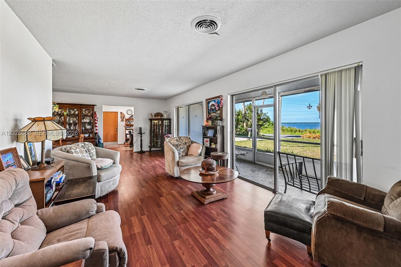 A living room with wood flooring, multiple armchairs, and a sliding door overlooking water — 7803 S Indian River, Fort Pierce FL 34982, FORT PIERCE, FL