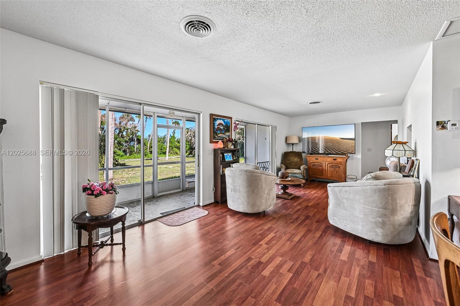 A living room features wood-look flooring, two light-colored armchairs, a television console, and sliding glass doors — 7803 S Indian River, Fort Pierce FL 34982, FORT PIERCE, FL