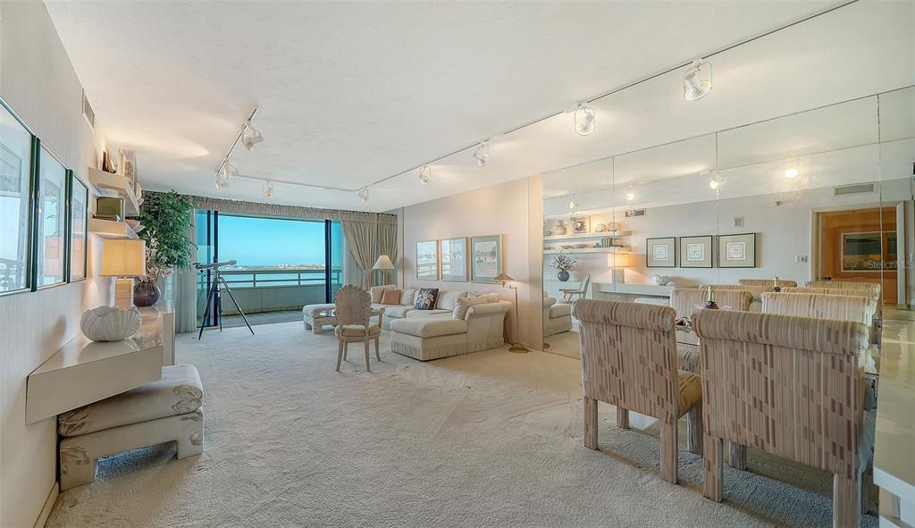 A living and dining room with beige carpet, track lighting, mirrored walls, and a balcony view — 988 BLVD OF THE ARTS UNIT 1411, SARASOTA, FL