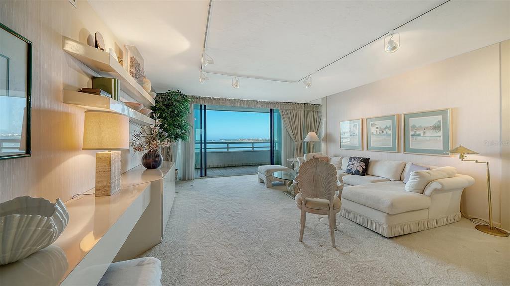 A living room with beige carpet, a white sectional sofa, and a balcony overlooking water — 988 BLVD OF THE ARTS UNIT 1411, SARASOTA, FL