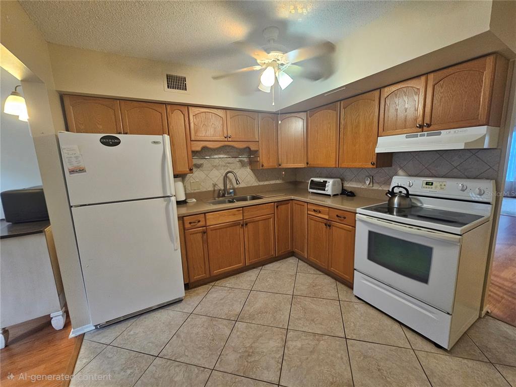 A kitchen features wood cabinets, white appliances, a ceiling fan, and light-colored tile flooring — 2469 FRANCISCAN DRIVE UNIT 59, CLEARWATER, FL