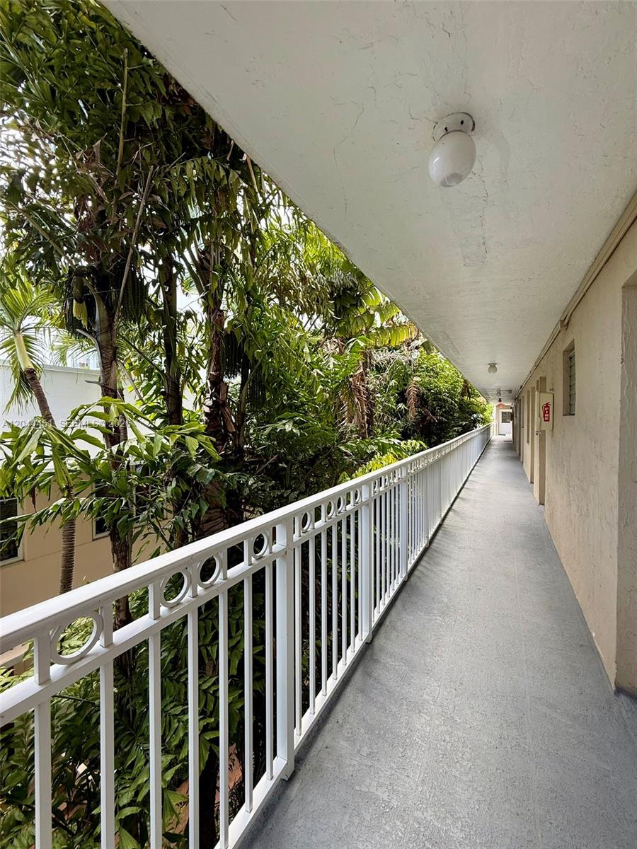 An outdoor walkway with a white metal railing overlooks lush green trees — 1575 Euclid Ave # 305, Miami Beach FL 33139, MIAMI BEACH, FL