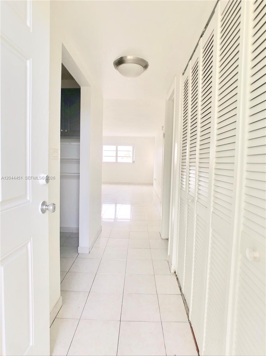 A hallway with white tile floors leads to a bright room with louvered closet doors — 1575 Euclid Ave # 305, Miami Beach FL 33139, MIAMI BEACH, FL