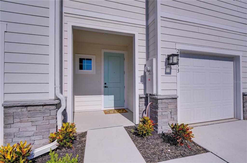 A light blue front door sits beside a white garage door on a house exterior — 20253 LOU ANGELA LANE, LUTZ, FL