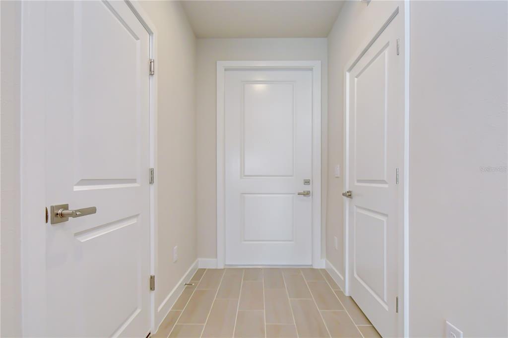 A hallway with light-colored tile flooring features three white doors and neutral walls — 20253 LOU ANGELA LANE, LUTZ, FL